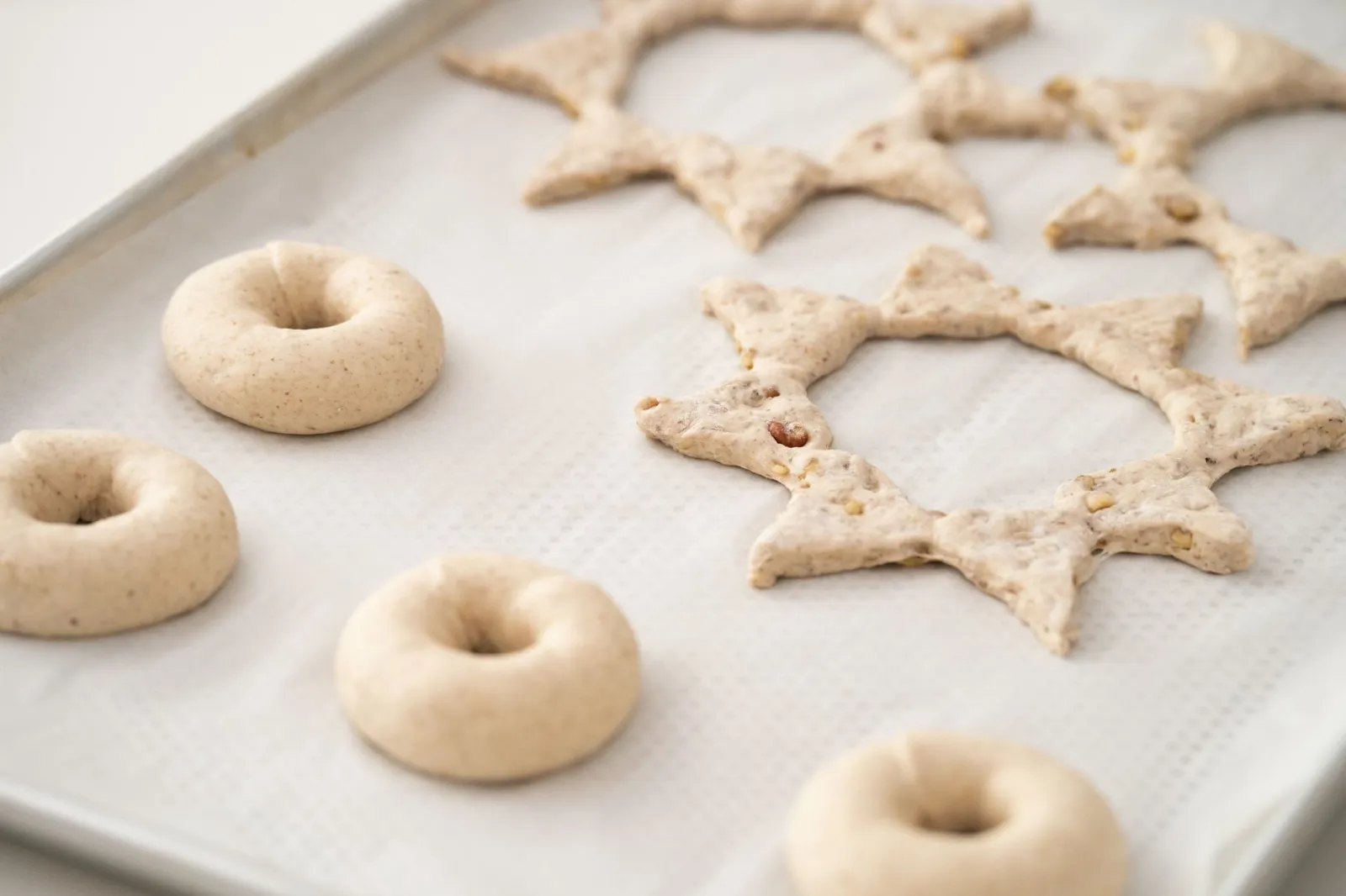 Close-up of homemade unbaked bagels and star-shaped pastries on a baking tray.